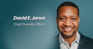 A close-up headshot of David Jones smiling brightly, against a teal backdrop with the words "David E. Jones, Chief Diversity Officer" on the backdrop